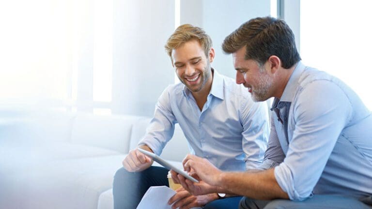 Young and mature businessmen smiling while using a digital tablet