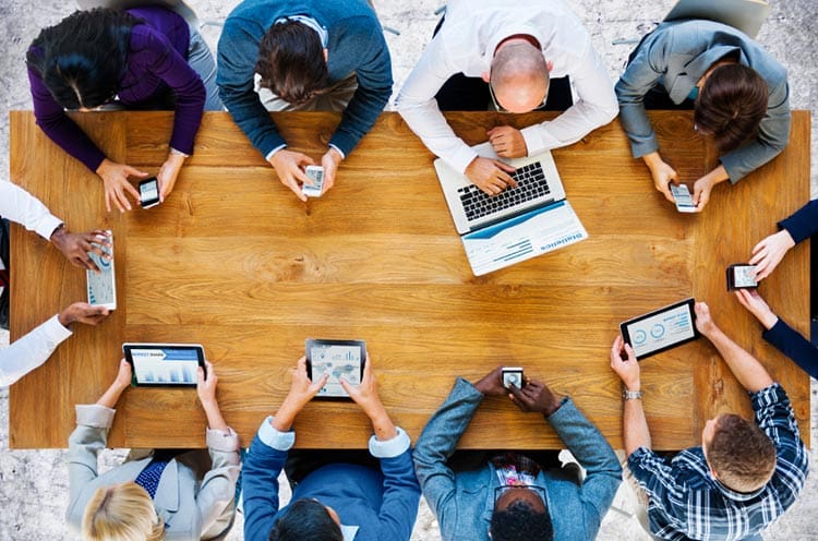 work employees sitting around a desk on phones and laptops