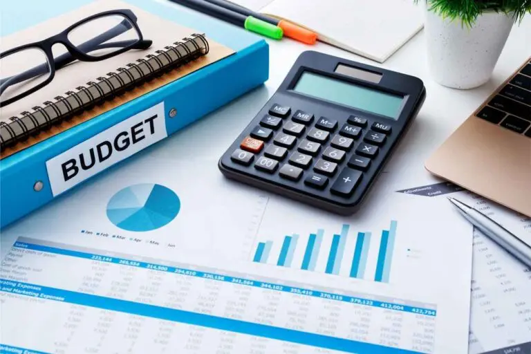 Desk with a binder that says "budget", glasses, calculator, and paper with graphs and charts.