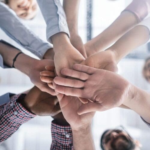 Team of colleagues stack their hands in the center to signify team work.
