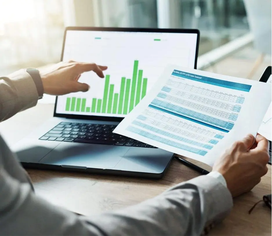 Male sitting at his desk with his laptop and a spreadsheet develops financial consulting solutions for businesses.